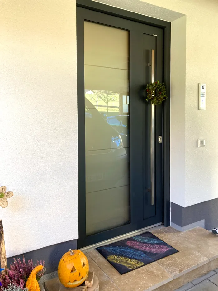 Moderne Haustür mit Glaseinsatz, Herbstkranz und geschnitztem Halloween-Kürbis auf der Fußmatte