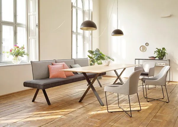 Moderner Essbereich mit Holztisch, gepolsterten Stühlen und Sofa vor großen Fenstern