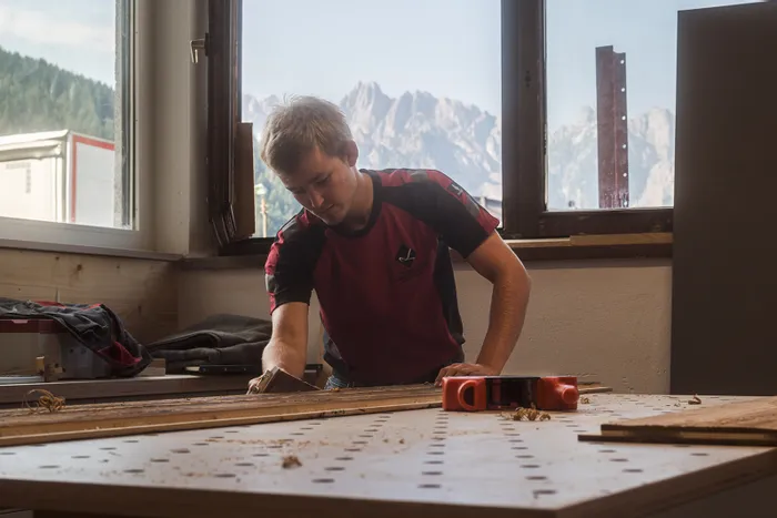 Tischler hobelt Holz in Werkstatt mit Bergblick durch Fenster
