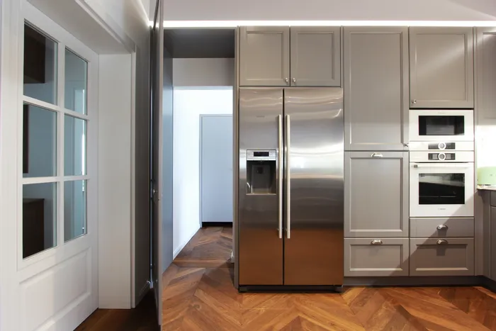 Moderne Küche mit grauen Einbauschränken und Edelstahl-Kühlschrank auf Fischgrät-Holzboden