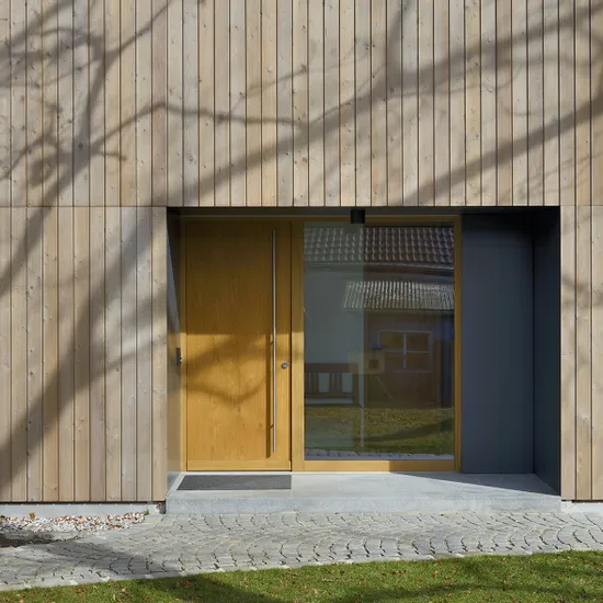 Moderne Holzfassade mit großer Eingangstür und Glasfront in Wohnsiedlung