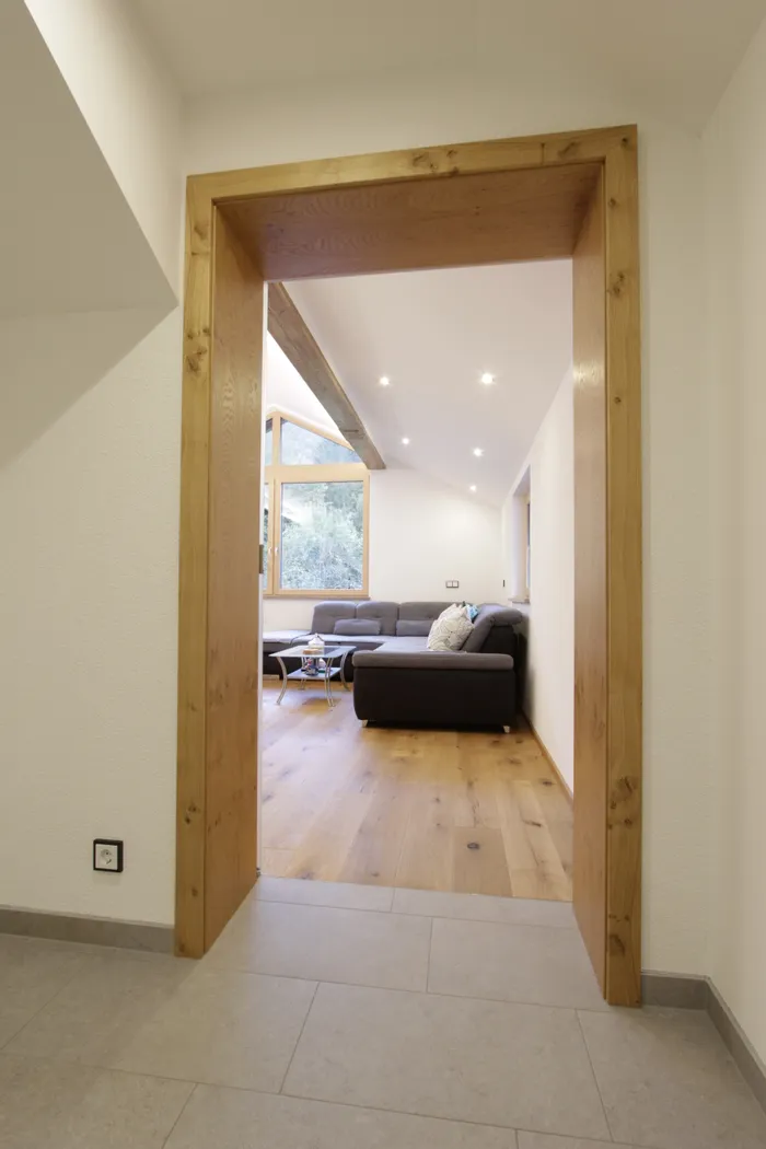 Helles Wohnzimmer mit Holzboden, Ecksofa und großem Fenster mit Blick ins Grüne