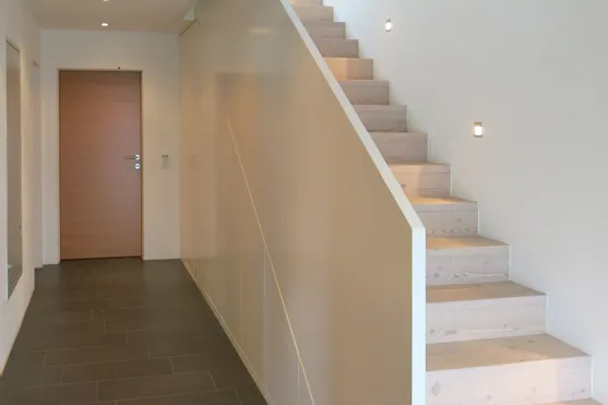 Moderne Innenflur mit dunklem Boden und heller Holztreppe mit seitlicher Beleuchtung