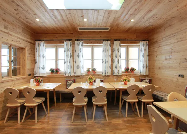 Gemütliches Restaurant mit Holzwänden, dekorierten Tischen und weißen Vorhängen im Alpenstil