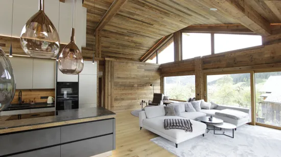 Modernes Chalet-Wohnzimmer mit offener Küche, Holzverkleidung und Panoramafenstern in den Alpen