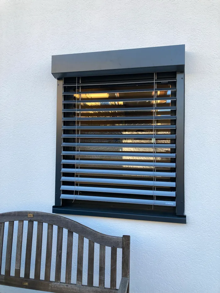 Außenjalousie an einem Fenster mit Holzbank davor an weißer Hauswand
