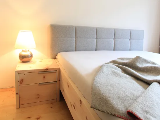 Modernes Schlafzimmer mit Holznachttisch, grauem Polsterbett und gefalteter Wolldecke