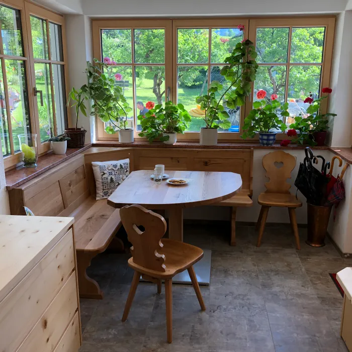 Gemütliche Essecke mit Holzmöbeln, großen Fenstern und Topfpflanzen mit Blick in den Garten