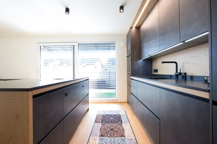 Moderne offene Küche mit dunklen Fronten, Holzboden und zentraler Kücheninsel bei Tageslicht