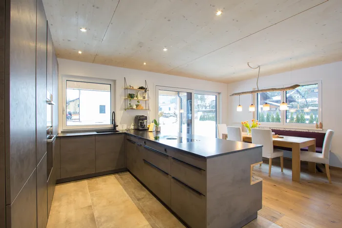 Moderne offene Küche mit Kochinsel, Essbereich und großen Fenstern mit Tageslicht