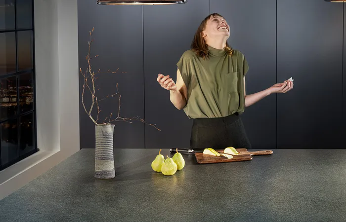 Frau lacht in moderner Küche mit Birnen auf Schneidebrett auf dunkler Stein-Arbeitsplatte