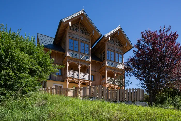 Traditionelles Holzhaus mit verzierten Balkonen auf Hügel unter blauem Himmel