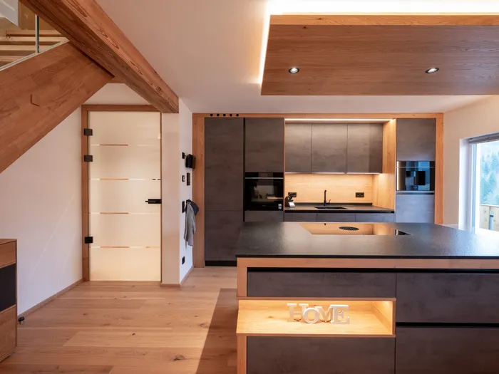 Moderne offene Küche mit Holzdetails, dunklen Fronten und Kücheninsel mit HOME-Dekoration