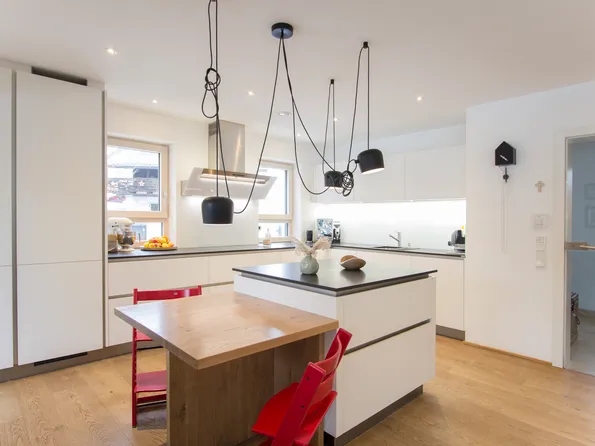 Moderne weiße Einbauküche mit Kücheninsel, Holzdetails und roten Stühlen auf Holzboden