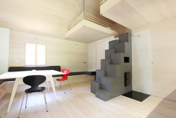 Helles minimalistisches Wohnzimmer mit Holzverkleidung, Esstisch, modernen Stühlen und grauem Treppenofen