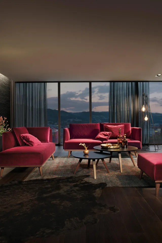 Modernes Wohnzimmer mit weinroten Samtmöbeln, dunklem Holzboden und Panoramablick bei Sonnenuntergang