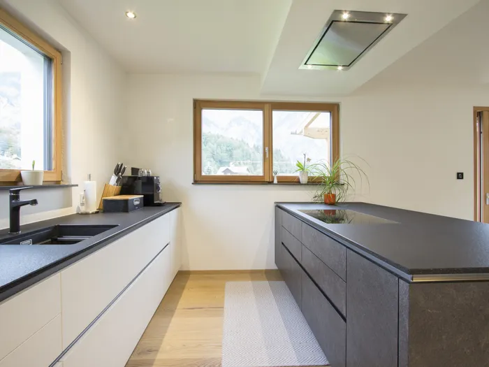 Moderne Einbauküche mit schwarzen Arbeitsplatten, Induktionskochfeld und Panoramafenstern