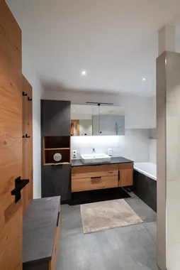 Modernes Badezimmer mit Holz- und Anthrazitmöbeln, Waschtisch und Badewanne