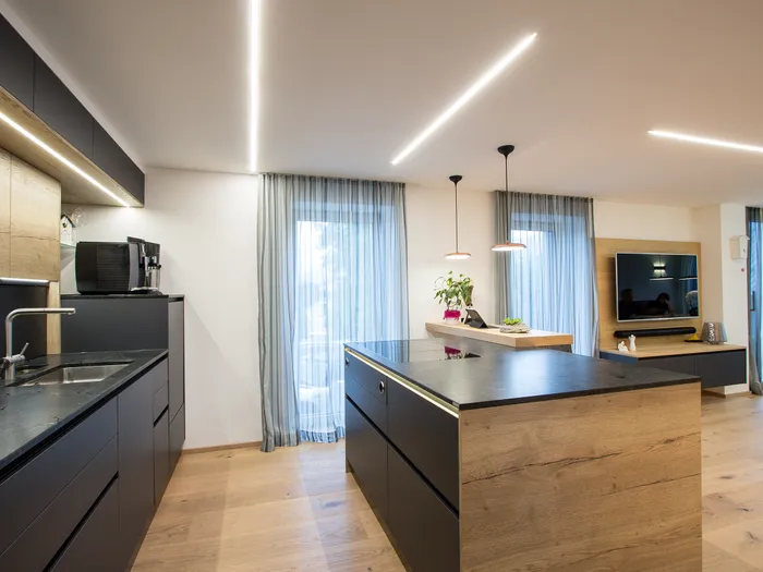 Moderne offene Küche mit Kochinsel, dunklen Fronten und Holzdetails sowie eingebautem TV-Bereich