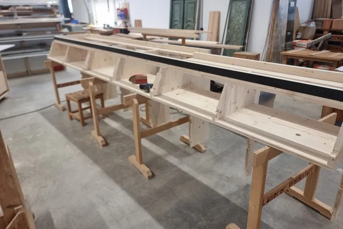 Holzkonstruktion in einer Tischlerwerkstatt mit Werkbänken und Werkzeugen im Hintergrund