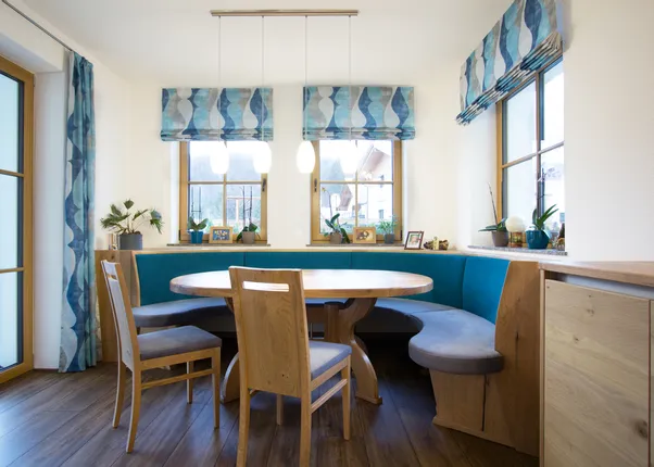 Gemütliche Essecke mit rundem Holztisch, blauer Polsterbank und Holzboden im modernen Landhausstil