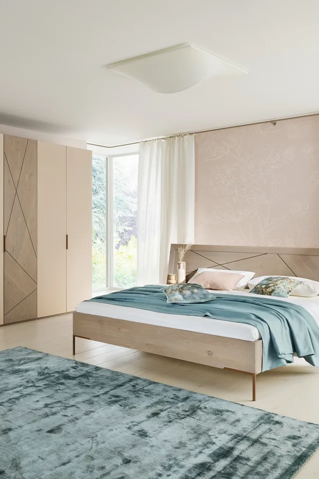 Modernes Schlafzimmer mit Holzbett, großem Kleiderschrank und türkisfarbenem Teppich im Tageslicht