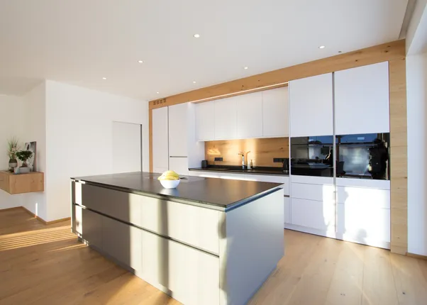 Moderne weiße Einbauküche mit Kochinsel, Holzverkleidung und natürlichem Lichteinfall