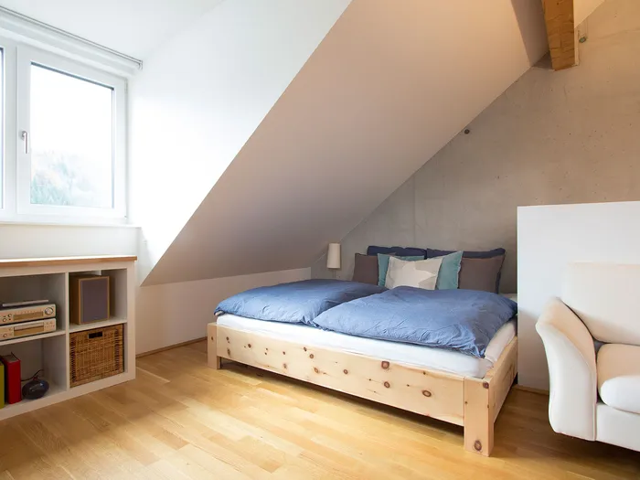 Gemütliches Schlafzimmer mit Dachschräge, Holzbett und blauer Bettwäsche