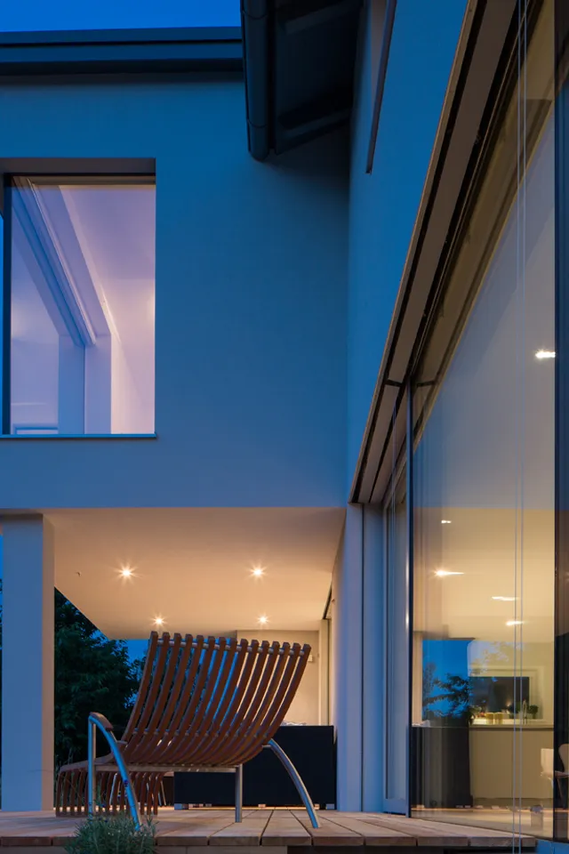 Moderne Villa mit Glasfassade und beleuchtetem Innenraum bei Abenddämmerung