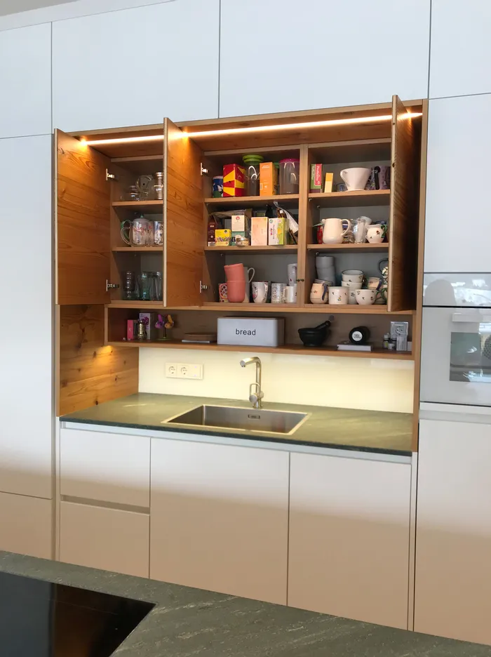 Moderne Küche mit offenem Hängeschrank voller Tassen, Gläser und Teeverpackungen