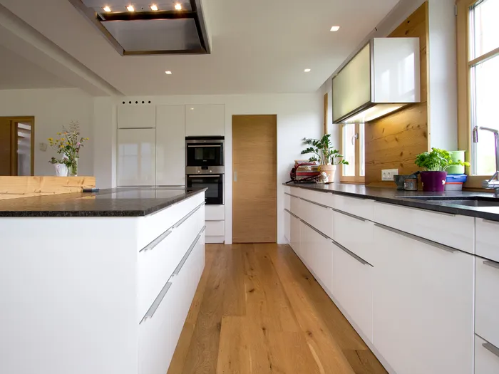 Moderne Küche mit weißen Hochglanzfronten, Holzfußboden und schwarzer Arbeitsplatte