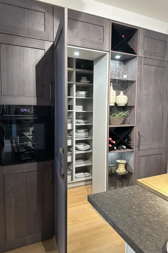 Moderne Küchenvorratskammer hinter dunkler Holzschranktür mit Regalen und Geschirr