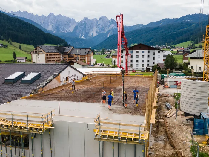 Bauarbeiter gießen Beton auf Baustelle in den Alpen mit Bergen im Hintergrund