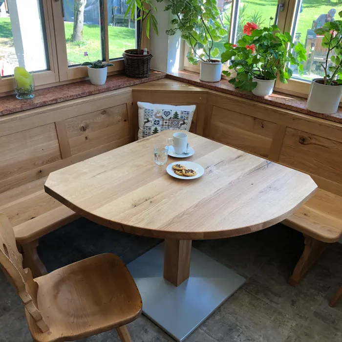 Gemütliche Holzeckbank mit Tisch und Stühlen vor Fenstern mit grünen Zimmerpflanzen