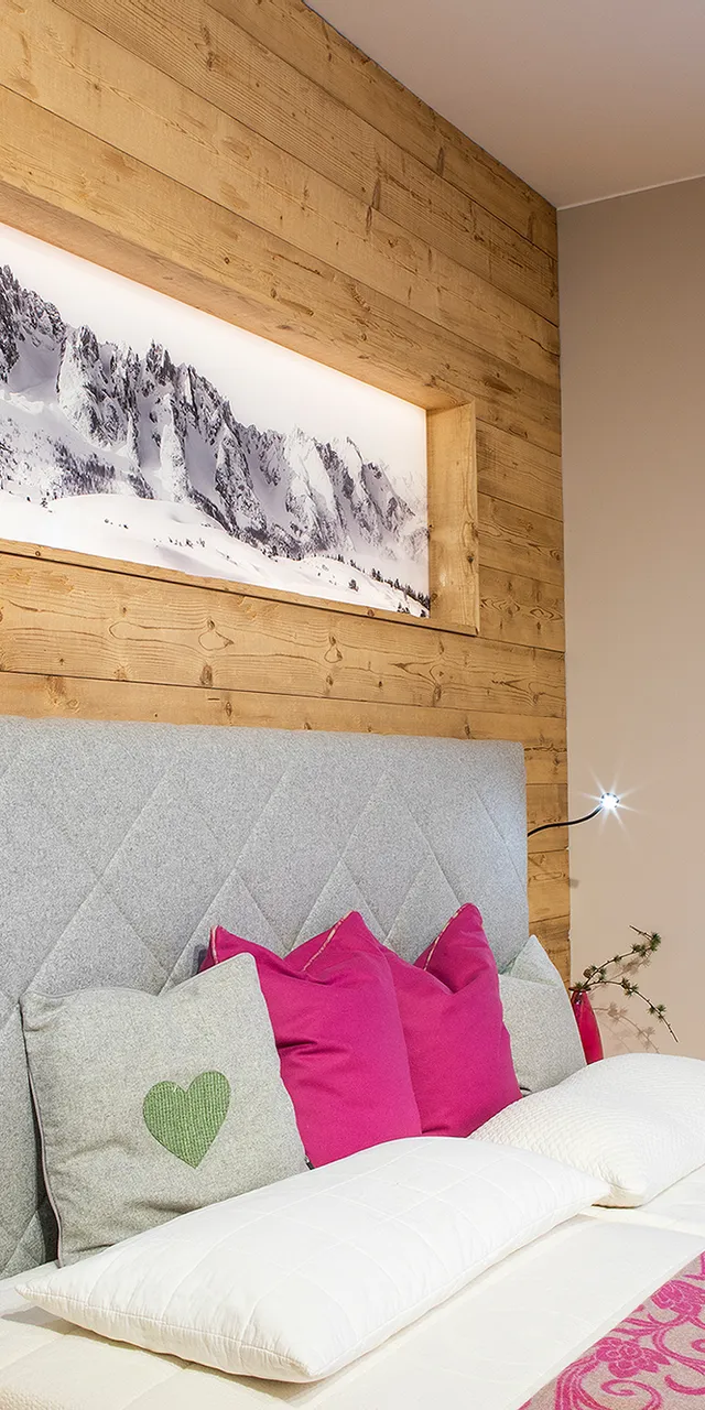 Modernes Schlafzimmer mit Holzwand, grauem Polsterbett, pinken Kissen und floralen Vorhängen