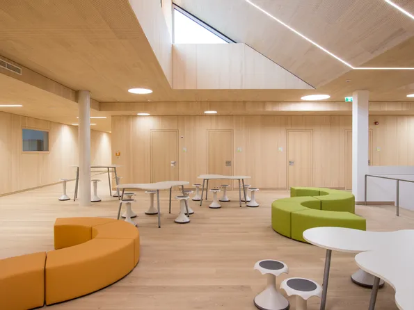 Heller Raum mit modernen Tischen, Hockern und farbigen Sitzbänken in Orange und Grün