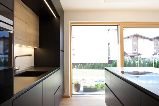 Moderne schwarze Einbauküche mit Holzfußboden und großem Fenster mit Gartenblick