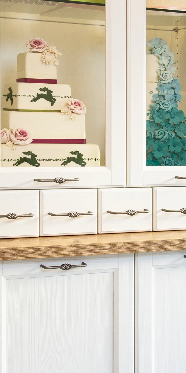 Ausstellung mit kunstvoll dekorierten Hochzeitstorten in einer Vitrine mit weißen Schränken