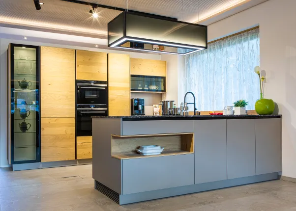 Moderne Küche mit Holzfronten, Kochinsel, Einbaugeräten und großen Fenstern mit Tageslicht