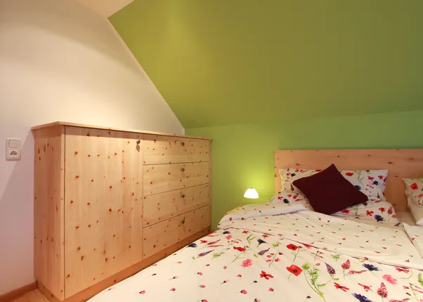 Gemütliches Schlafzimmer mit Blumenbettwäsche, grün gestrichener Wand und Möbeln aus hellem Holz