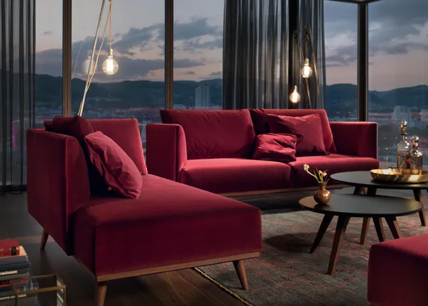 Modernes Wohnzimmer mit dunkelroten Samtsofas vor Panoramafenstern bei Sonnenuntergang