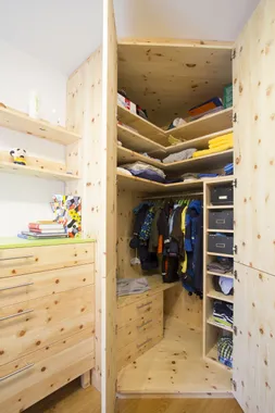 Offener Kleiderschrank aus hellem Holz mit Kleidung, Regalen und Schubladen in einem Kinderzimmer