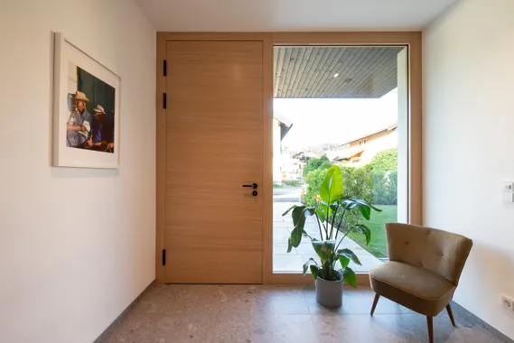 Moderne Diele mit Holz-Eingangstür, großem Fenster, Zimmerpflanze und Sessel