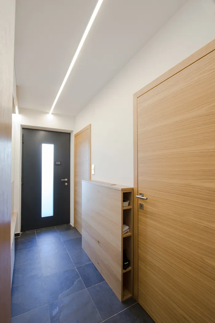 Moderner Flur mit hellen Holztüren, dunklen Bodenfliesen und LED-Deckenbeleuchtung