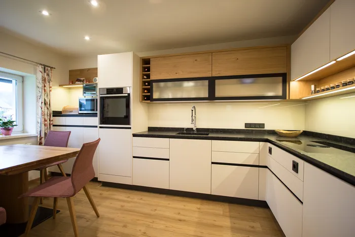 Moderne Einbauküche mit weißen Fronten, Holzdetails und schwarzer Arbeitsplatte