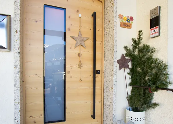 Holzeingangstür mit Weihnachtsdeko, Geschenk, Fussmatte und kleiner Tanne daneben