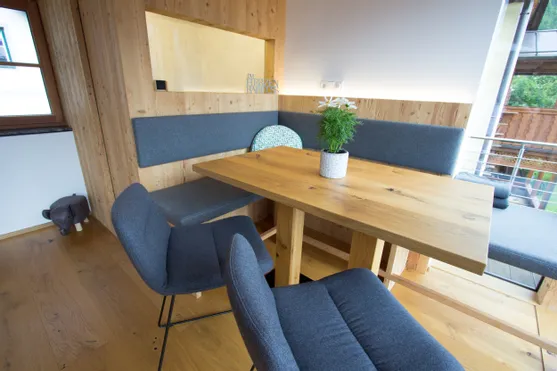 Moderne gemütliche Essecke mit Holztisch, grauen Polsterbänken und Zimmerpflanze