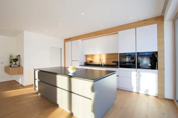 Moderne weiße Einbauküche mit Kochinsel, Holzverkleidung und natürlichem Lichteinfall
