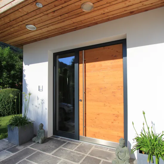 Moderne Haustür aus Holz mit Glasrahmen, flankiert von Pflanzen und Buddha-Statuen