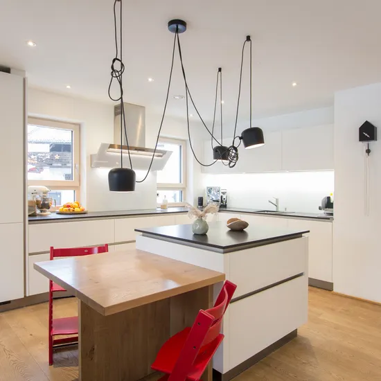 Moderne weiße Einbauküche mit Kücheninsel, Holzdetails und roten Stühlen auf Holzboden